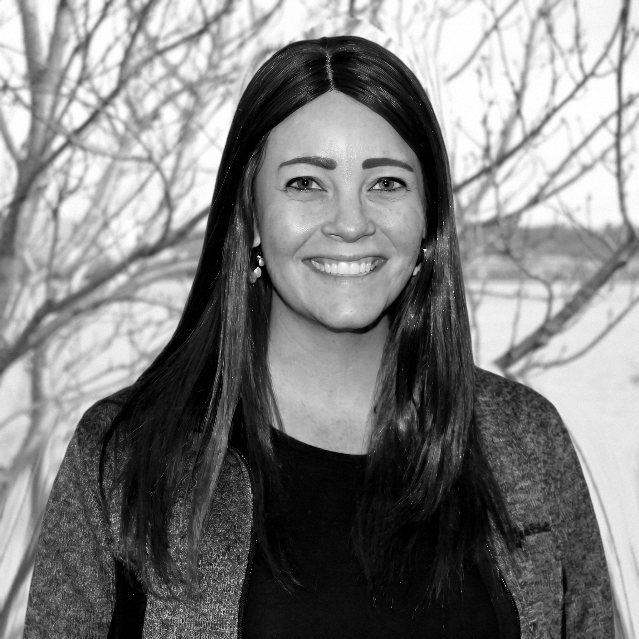 Smiling woman outdoors in black and white, with bare tree branches in the background.