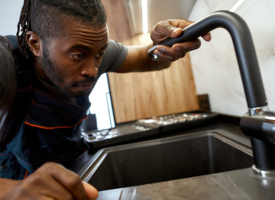 Closeup portrait African plumber holding kitchen tap Close portrait professional African American plumber fixing black water tap in kitchen, holding it with one hand.Young stylish handyman over kitchen sink.