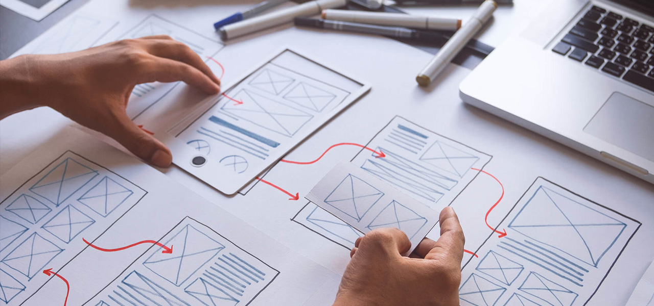Designer sketching website wireframes on paper at a desk